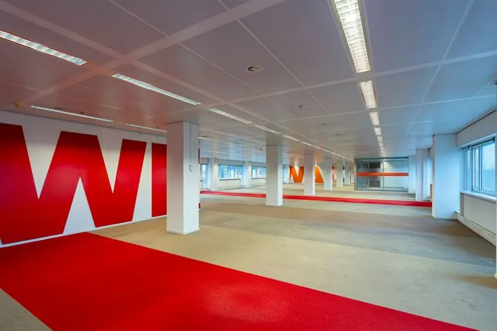 Ruime, modern ingerichte kantoorruimte aan de Europalaan met roodtapijt en grote ramen voor natuurlijk licht.