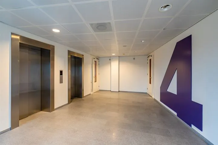 Moderne lifthal met twee liften en een groot paars cijfer 4 op de muur in een kantoorgebouw aan de Europalaan.