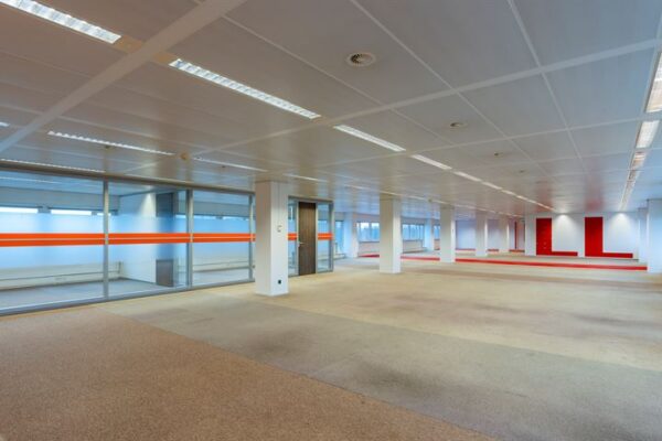 Ruime, leegstaande kantoorruimte aan de Europalaan met glazen wanden en rode accenten op de muren.