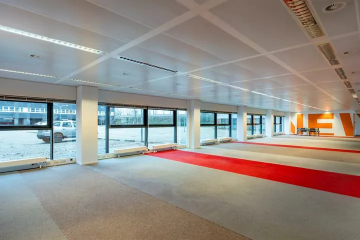 Lege kantoorruimte aan de Europalaan met grote ramen en roodgrijze vloerbedekking.