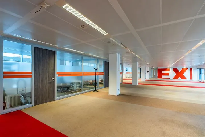 Moderne, lege kantoorruimte aan de Europalaan met glazen vergaderruimtes en grote rode EXIT-belettering op de achterwand.