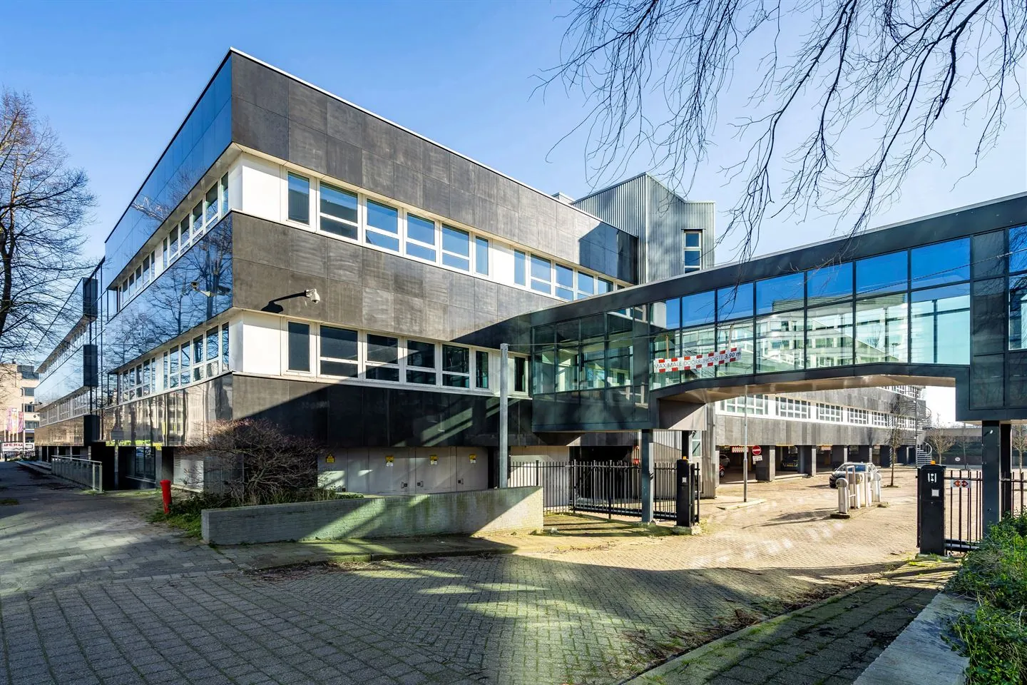 Modern kantoorgebouw aan de Eendrachtlaan met glazen loopbrug en parkeerterrein op de voorgrond.