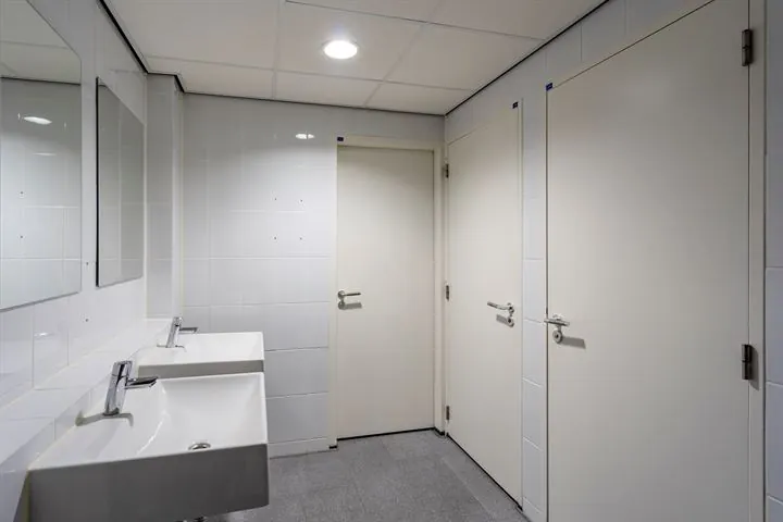 Wit betegelde toiletruimte in een kantoorpand aan de Eendrachtlaan met twee wastafels en drie gesloten deuren.