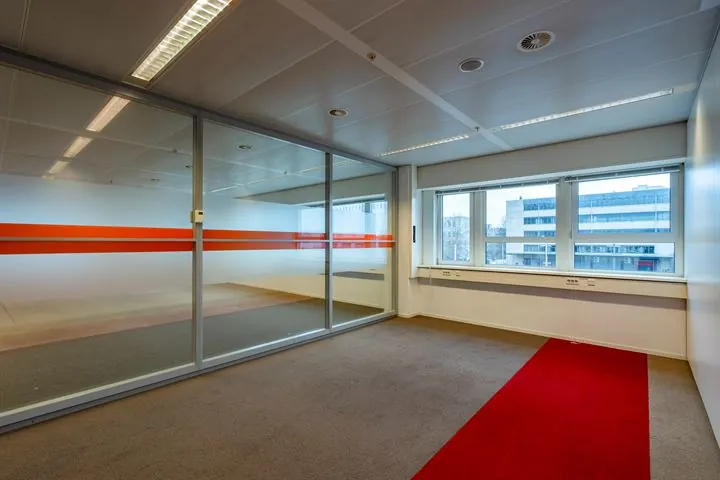 Kantoorruimte aan de Eendrachtlaan met glazen wanden, rood vloeraccent en uitzicht op omliggende kantoorgebouwen.
