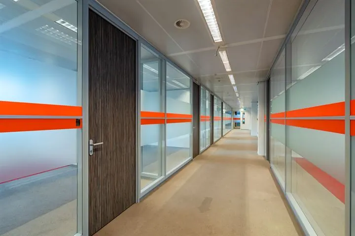 Gang in een modern kantoorpand aan de Eendrachtlaan met glazen wanden en horizontale oranje accenten.