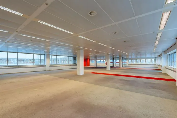 Ruime, lege kantoorverdieping aan de Eendrachtlaan met grote ramen en rode accenten op de vloer.