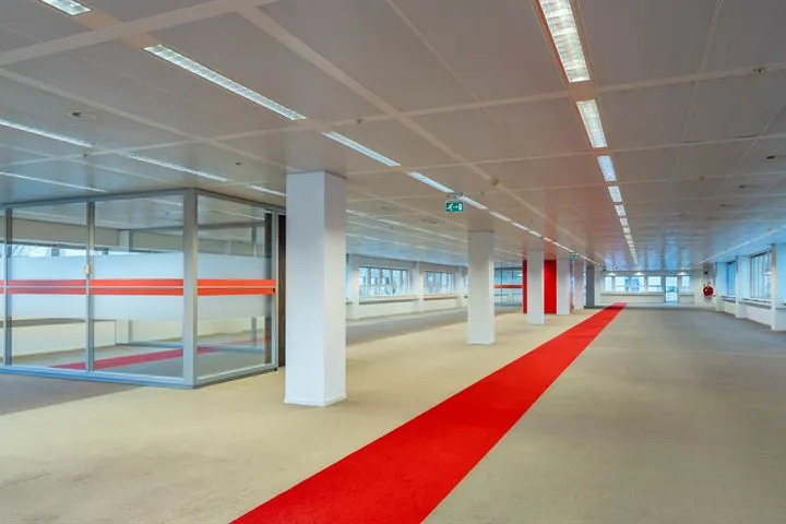 Ruim, leeg kantoorgebouw aan de Eendrachtlaan met glazen vergaderruimte en rode loper over de vloer.