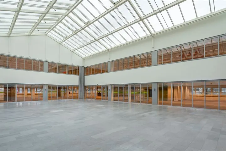 Ruime, lichte atriumruimte in een modern kantoorgebouw aan de Eendrachtlaan met glazen dak en rondom glazen wanden.
