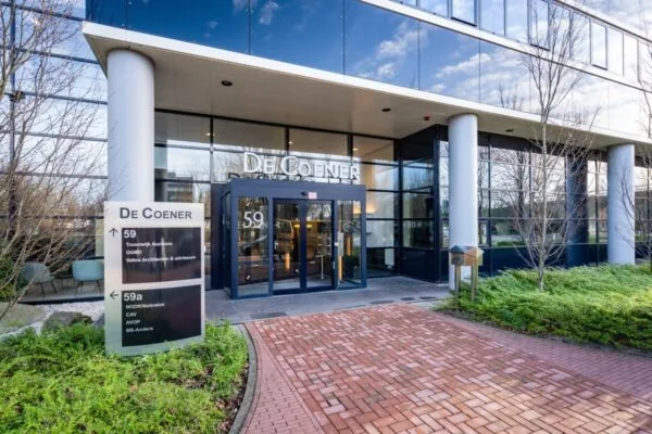 Ingang van het kantoorpand De Coener aan de Overschiestraat 59 met bedrijfsnaambord in de voortuin.
