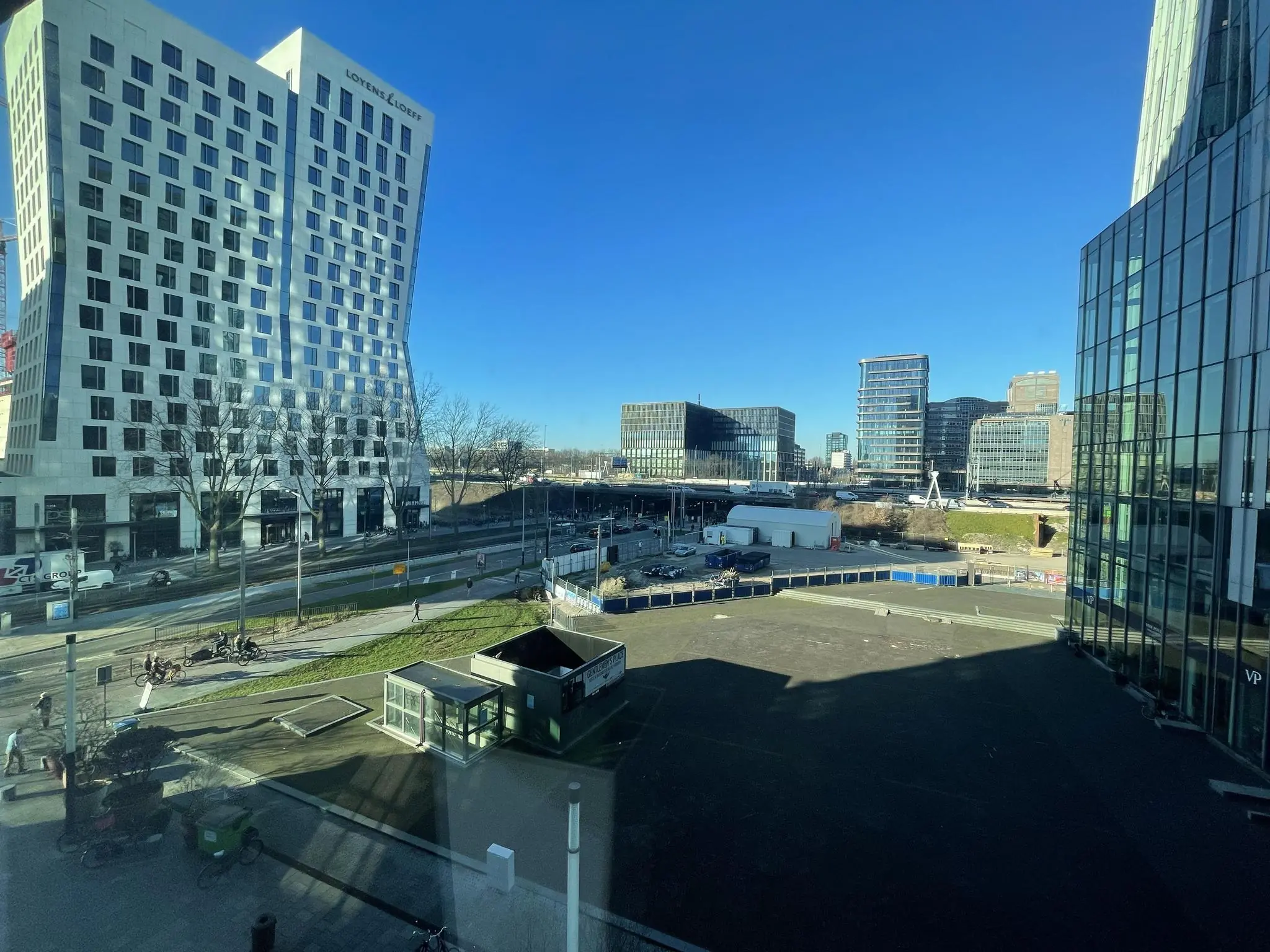 Zicht op de Parnassusweg in Amsterdam met het kantoorgebouw Loyens & Loeff en omliggende moderne hoogbouw op een zonnige dag.