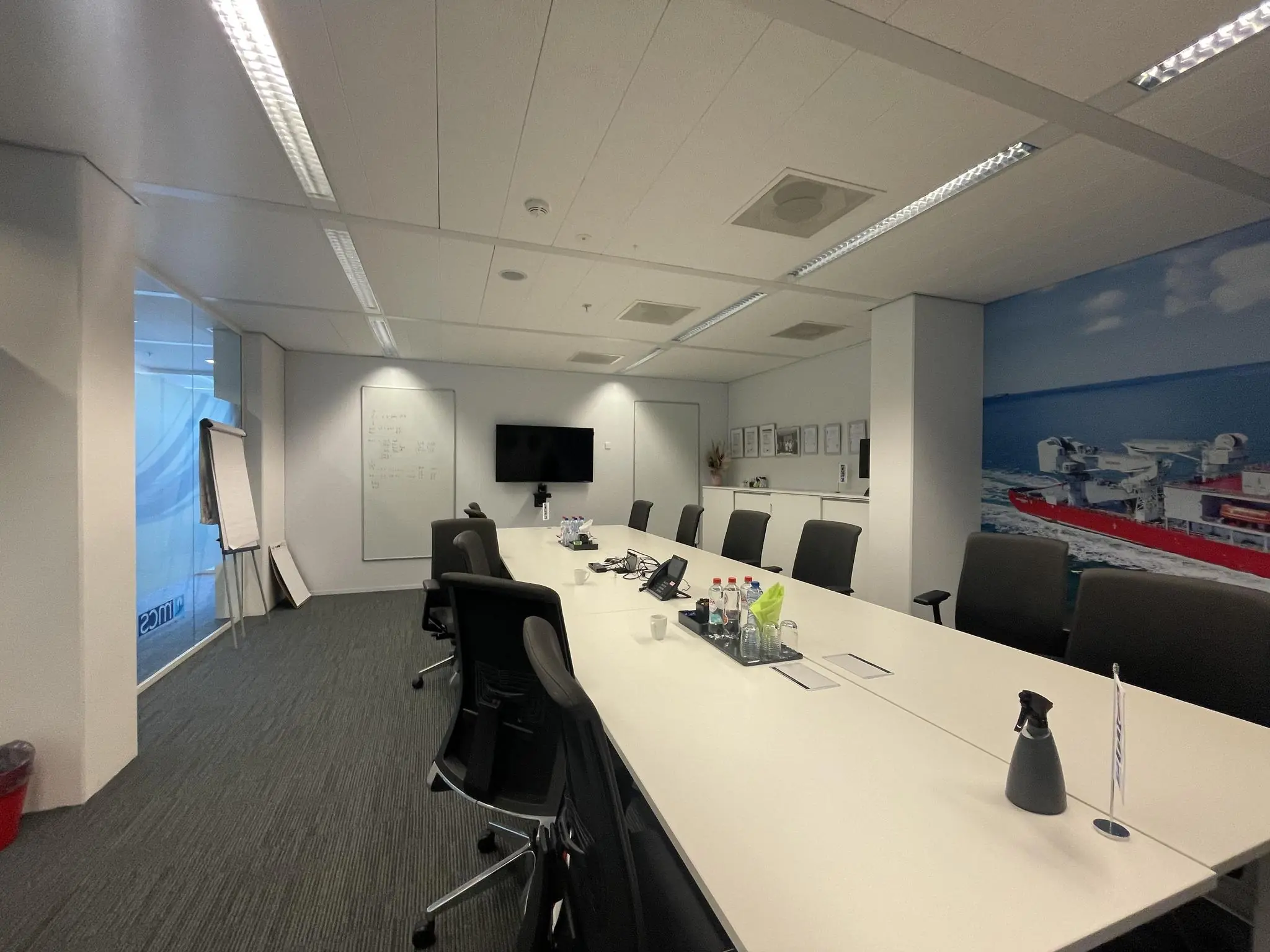 Vergaderruimte aan de Parnassusweg met lange tafel, stoelen, presentatiescherm en een muurfoto van een rood schip op zee.