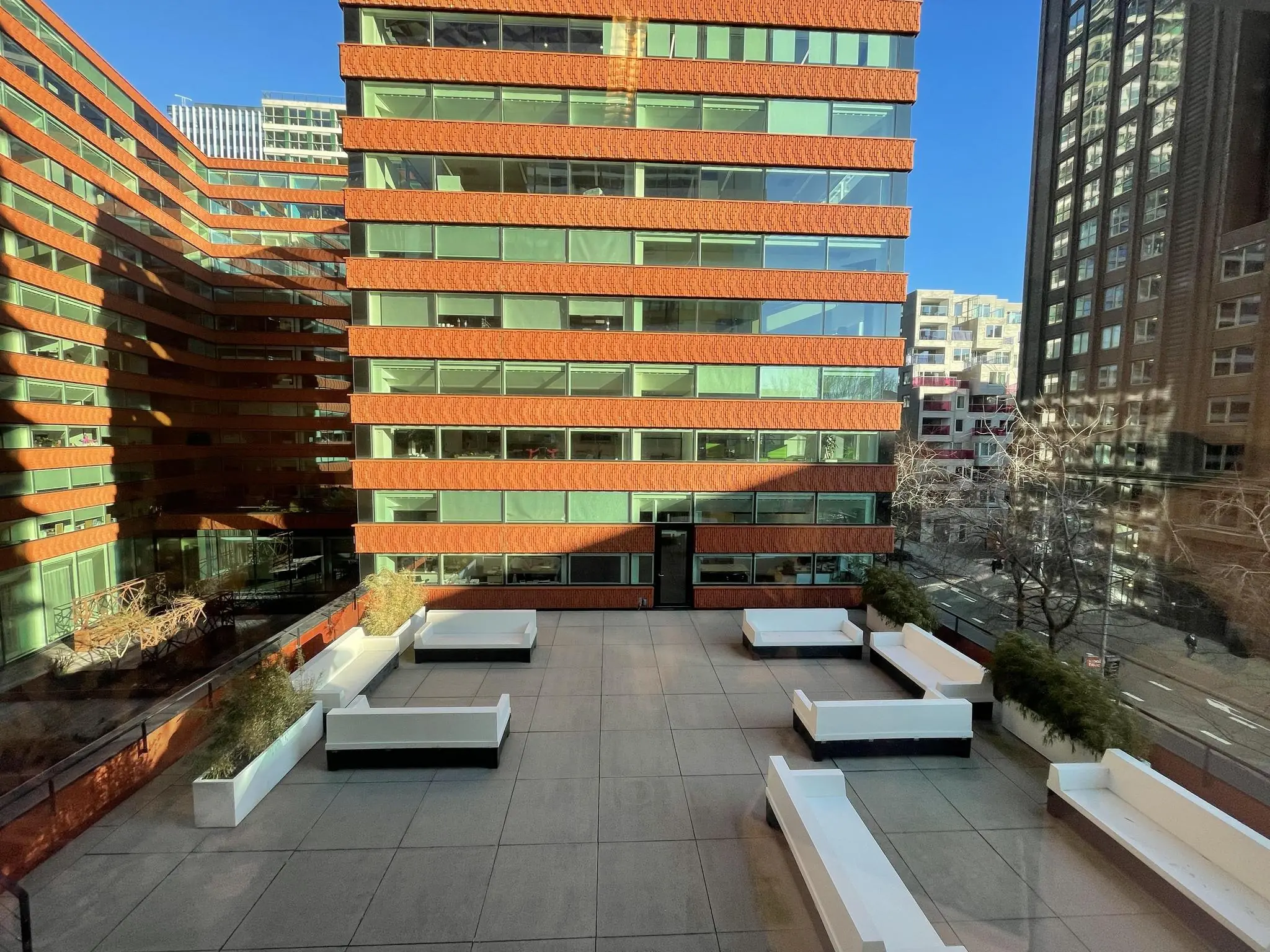Moderne binnentuin met witte loungebanken aan de Parnassusweg, omringd door hoge kantoorgebouwen met rood-oranje gevels.