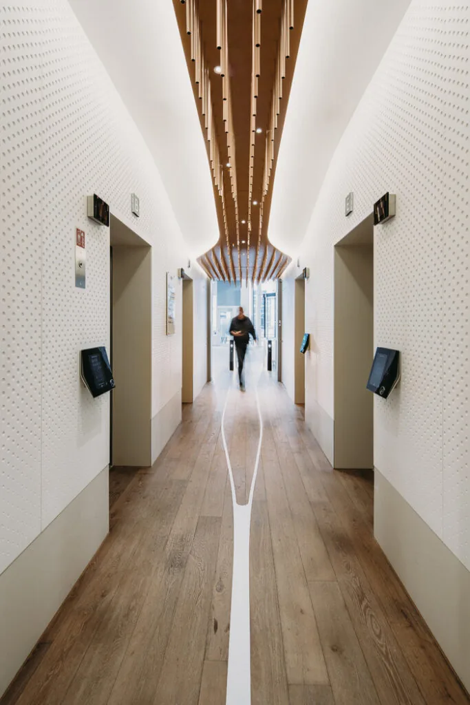 Moderne liftlobby aan de Parnassusweg met houten vloer, strak wit design en houten plafondaccenten.