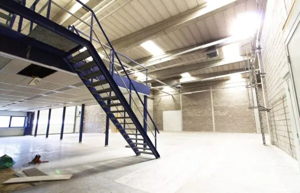 Ruime, lege bedrijfshal aan de Zonnebaan met metalen trap naar verdiepingsvloer.