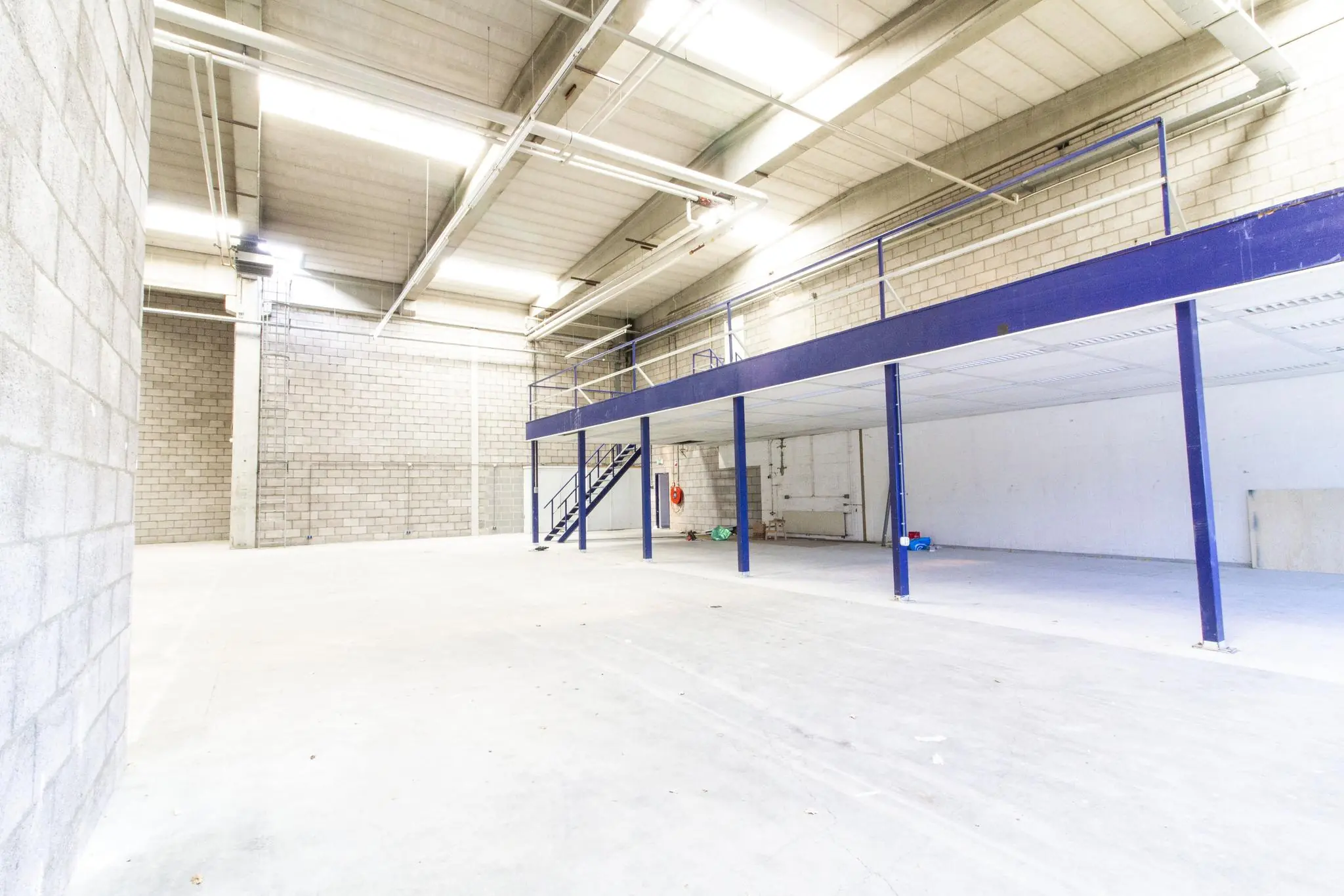 Licht en ruim magazijn aan de Zonnebaan met een entresol en betonnen muren.