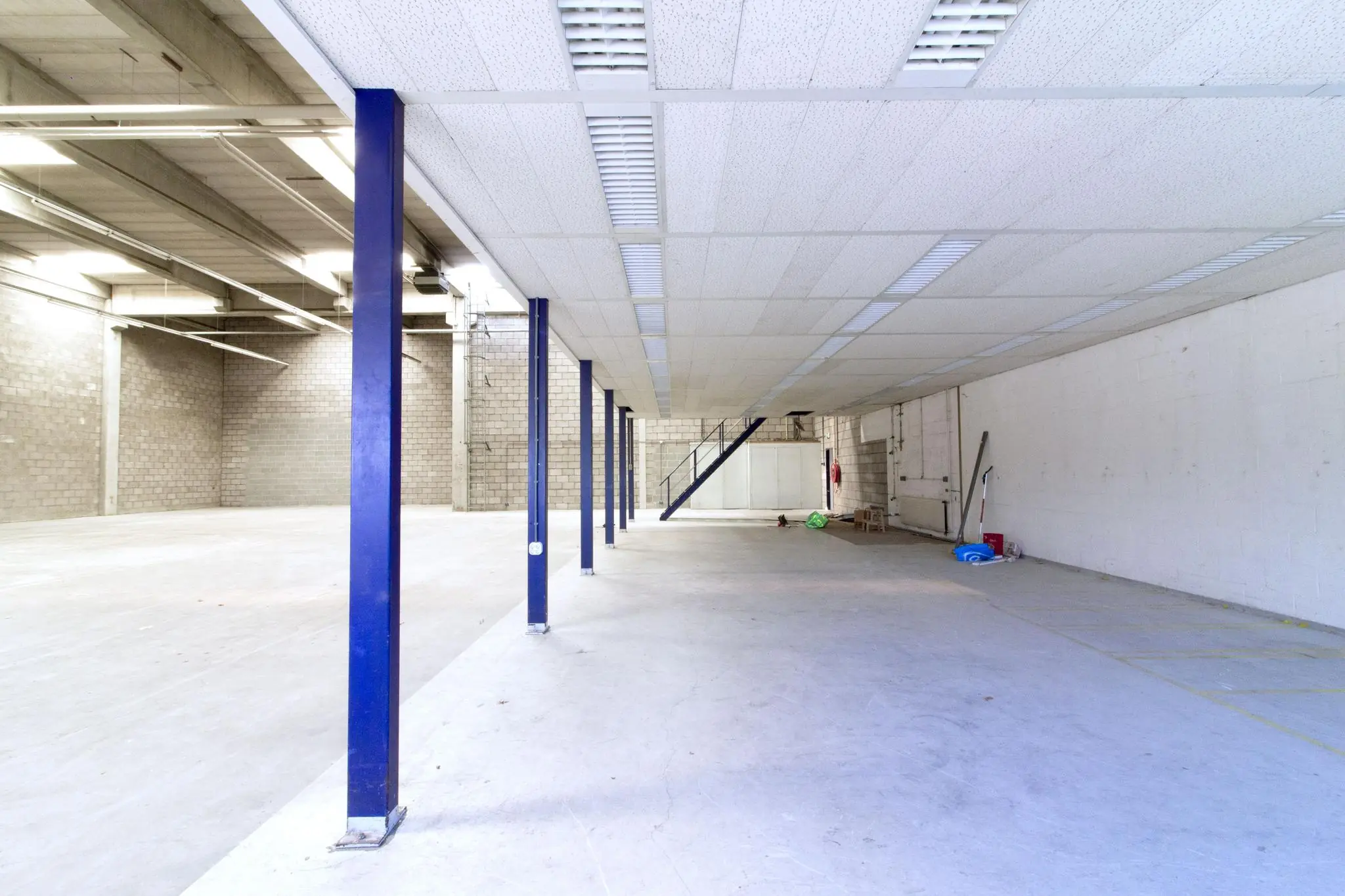 Leegstaand bedrijfs- of opslagpand aan de Zonnebaan met betonnen vloer, blauwe steunpilaren en een entresolvloer met trap.