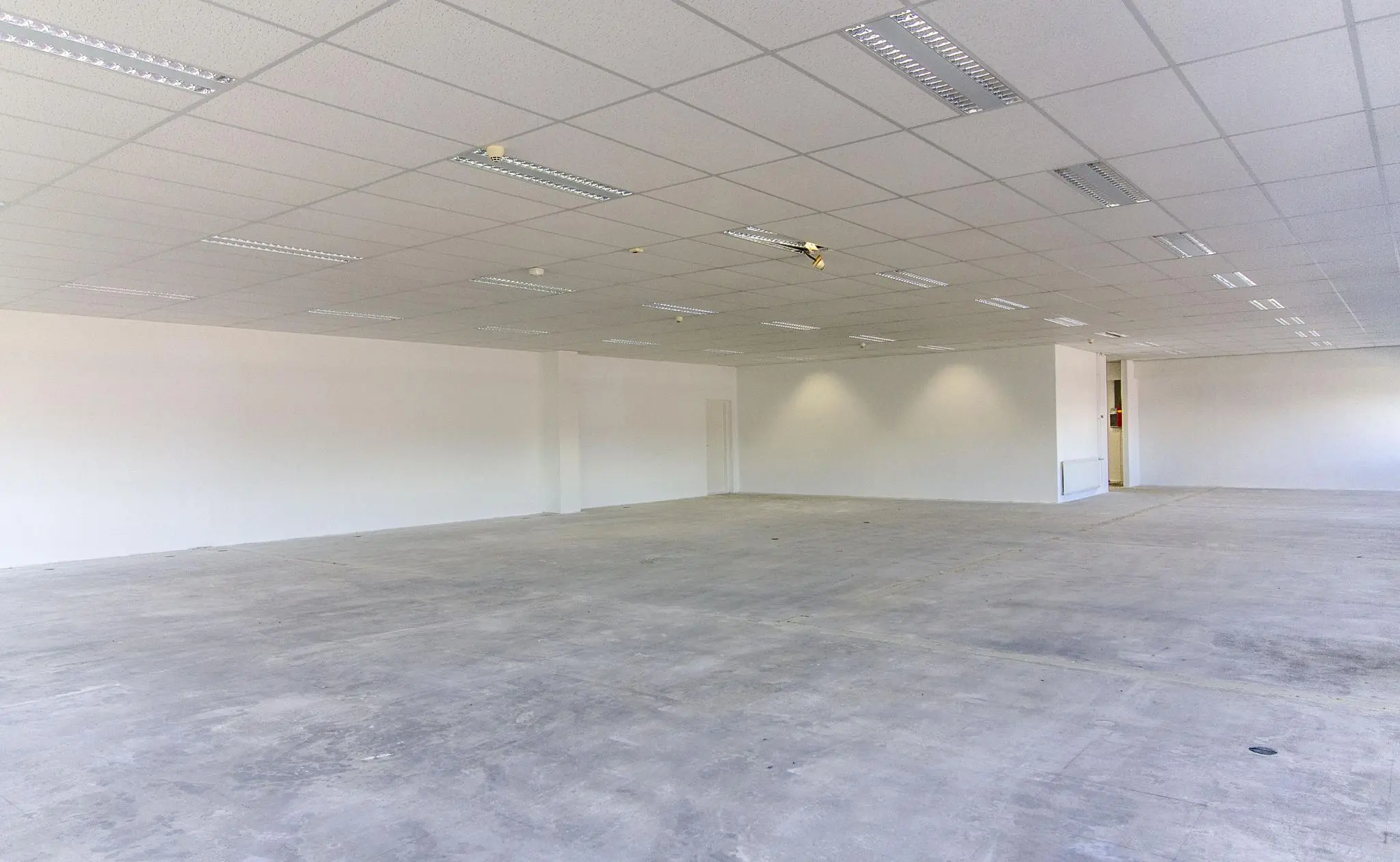 Leeg, witgeschilderd bedrijfspand met systeemplafond en betonnen vloer aan de Zonnebaan.