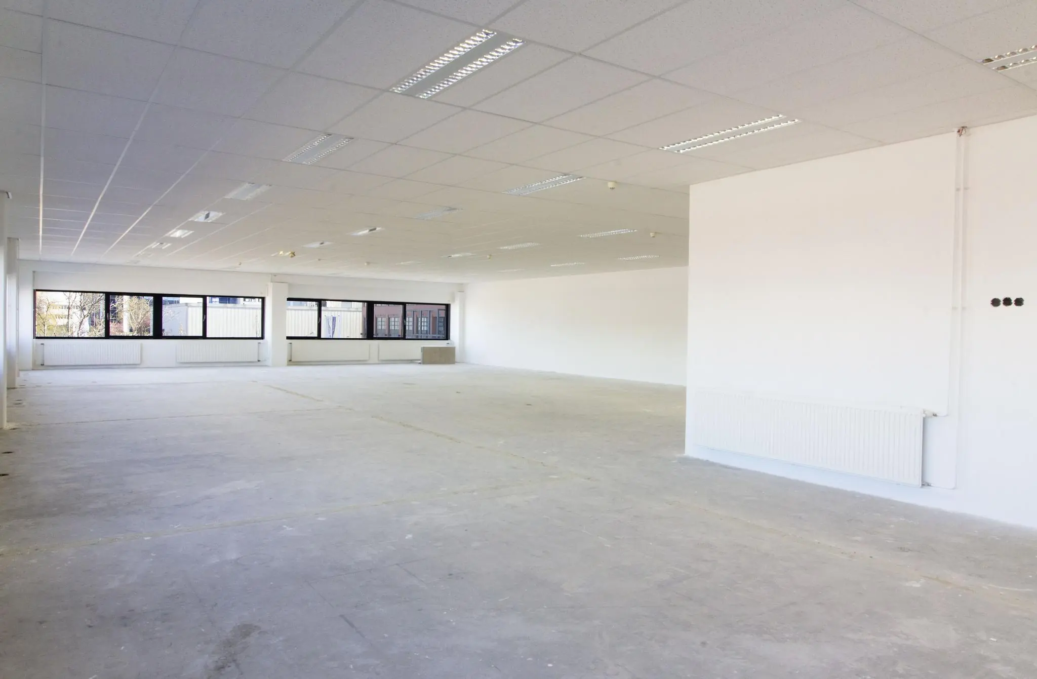 Leegstaand kantoorruimte op de Zonnebaan met witte wanden, systeemplafond en grote ramen.