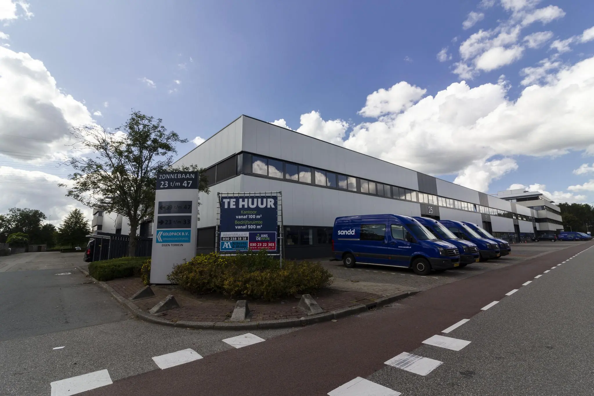 Bedrijventerrein aan de Zonnebaan met te huur-bord en geparkeerde blauwe Sandd-busjes voor een modern bedrijfsgebouw.