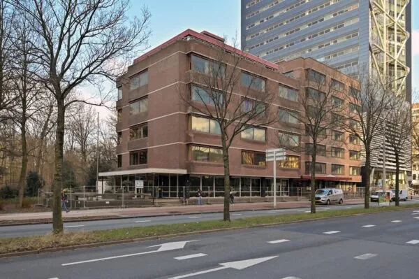 Bakstenen kantoorpand aan de Bezuidenhoutseweg in Den Haag met op de achtergrond een moderne hoogbouwtoren.