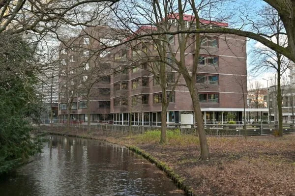 Kantoorgebouw aan de Bezuidenhoutseweg in Den Haag, gezien vanaf de overkant van een waterpartij met bomen op de voorgrond.