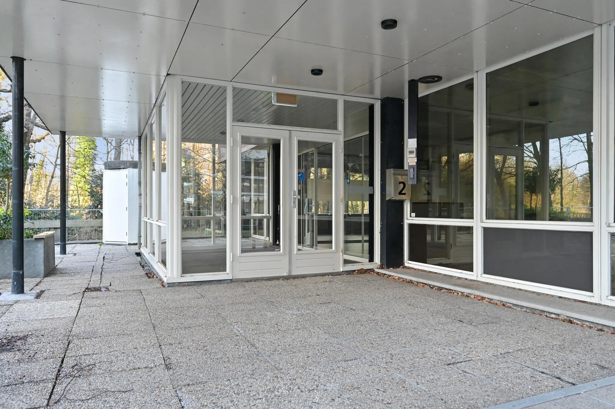 Ingang van een modern kantoorpand aan de Bezuidenhoutseweg met glazen deuren en betonnen terras.