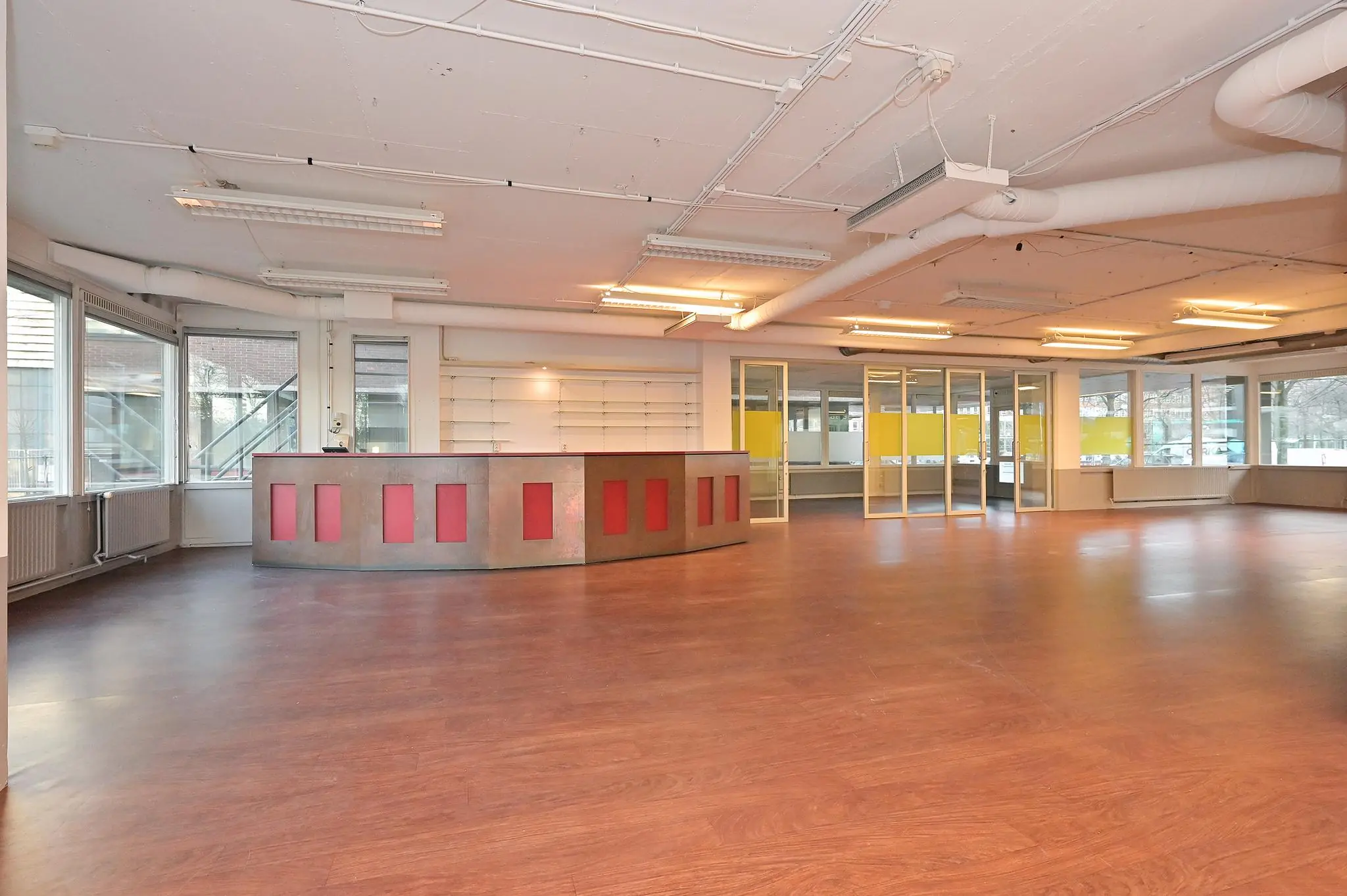 Ruime, lege kantoorruimte aan de Bezuidenhoutseweg met houten vloer, balie en grote raampartijen.