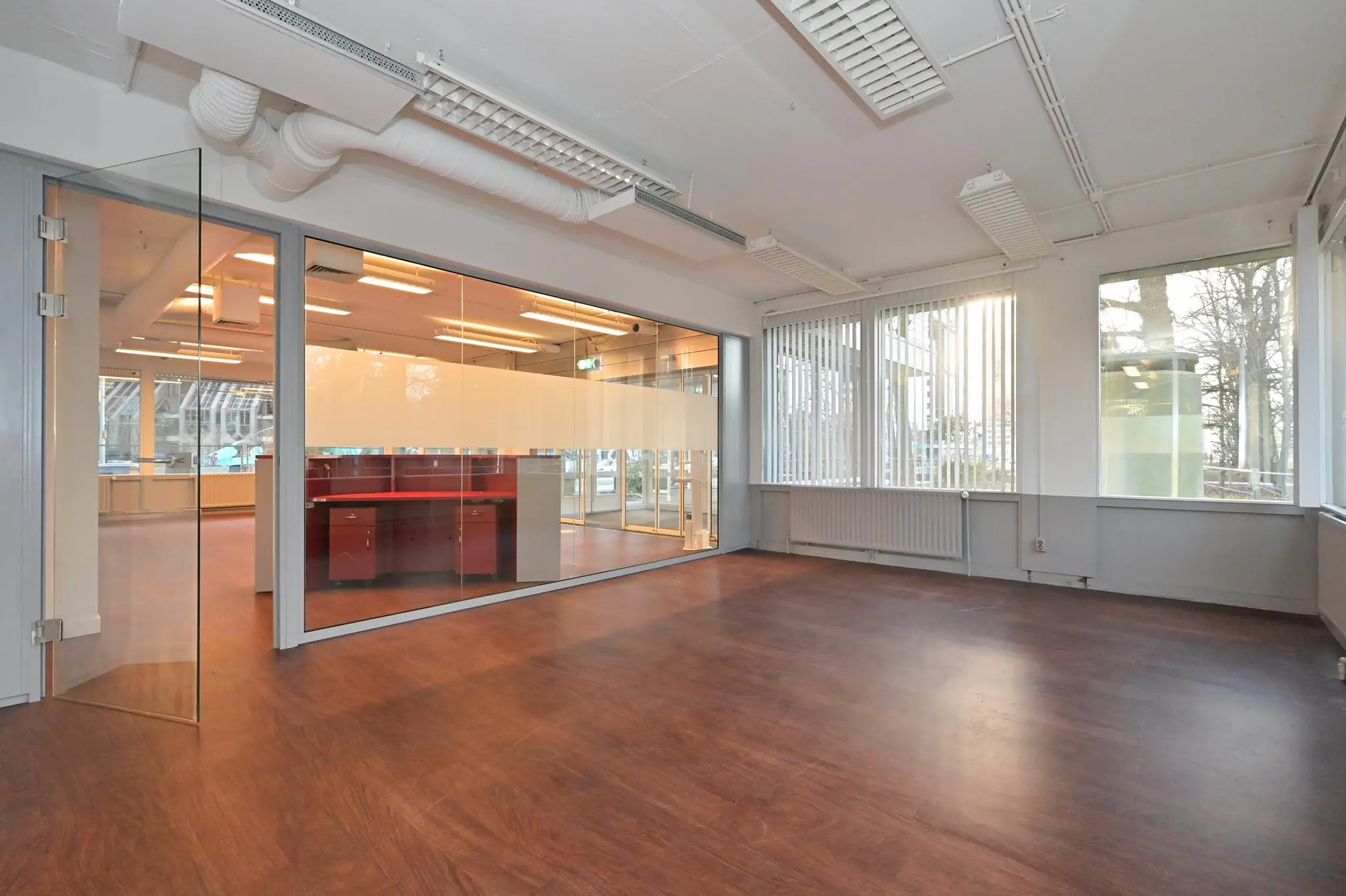 Licht en modern kantoorruimte aan de Bezuidenhoutseweg met glazen scheidingswand en houten vloer.