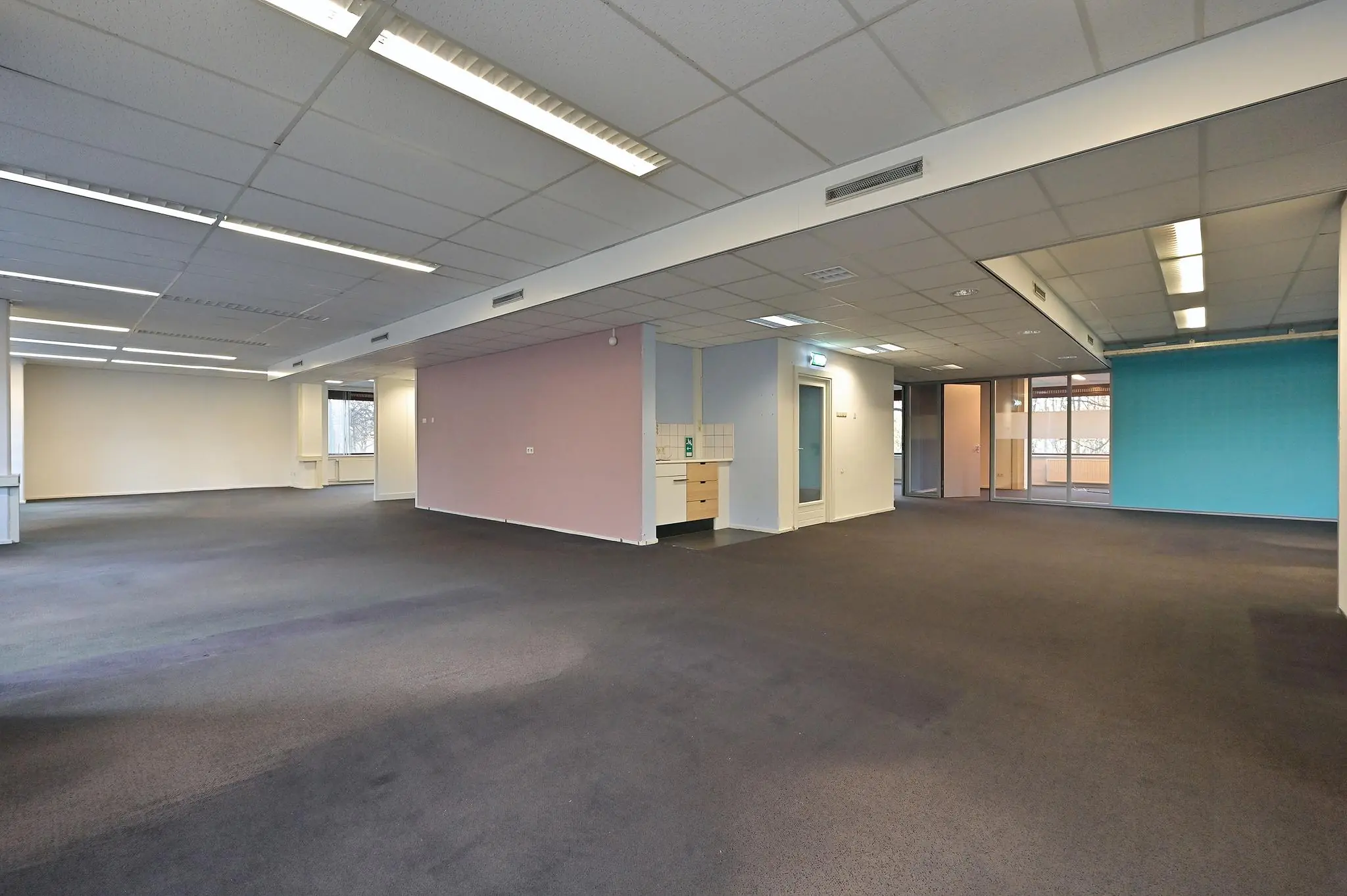 Ruime, leegstaande kantoorruimte aan de Bezuidenhoutseweg met gekleurde wanden en systeemplafond.