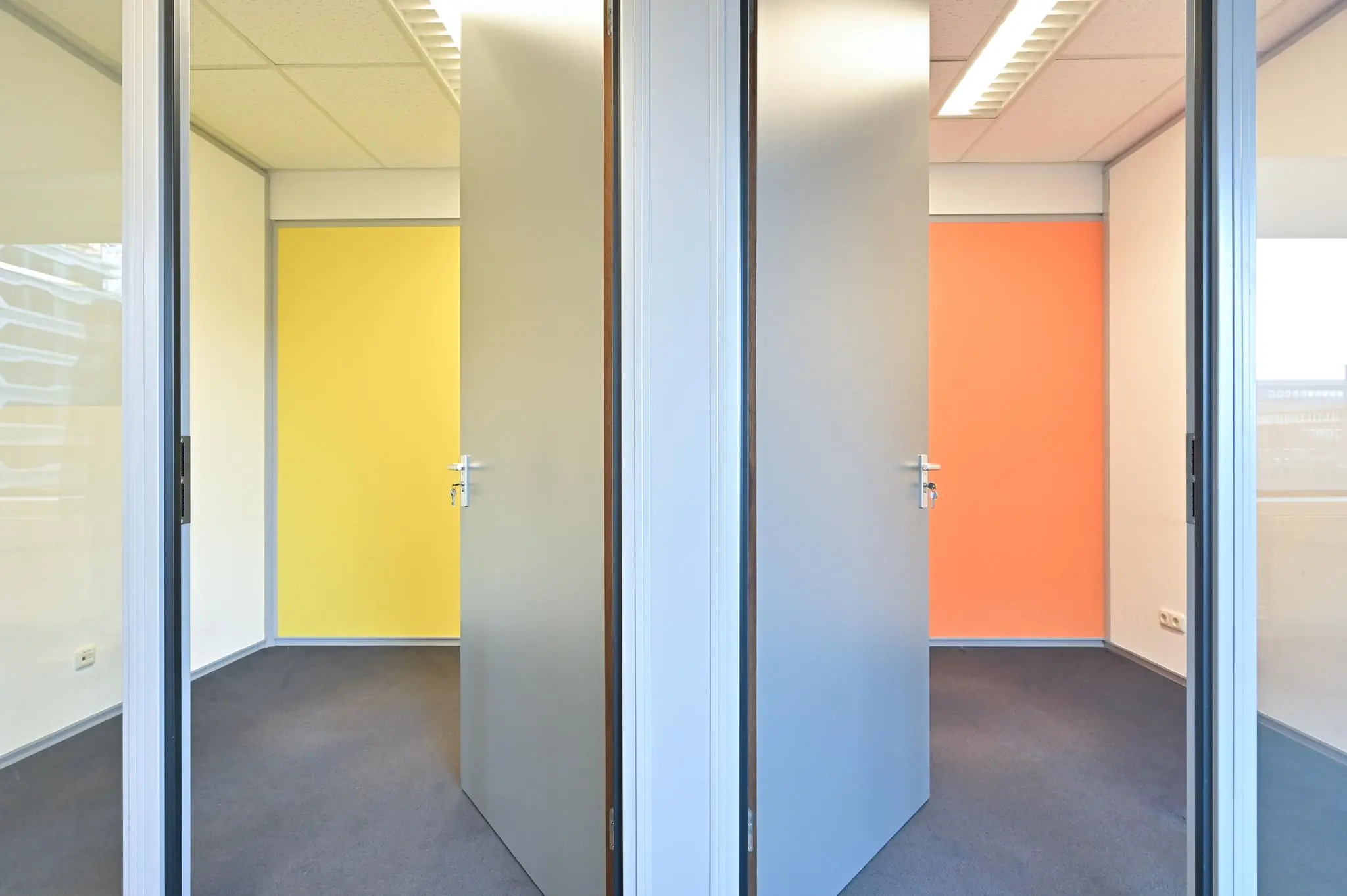 Twee openstaande deuren in een kantoorruimte aan de Bezuidenhoutseweg, met een gele en een oranje achterwand.