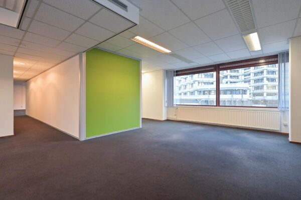 Leeg kantoorruimte aan de Bezuidenhoutseweg met een groen accentmuur en groot raam met uitzicht op moderne gebouwen.
