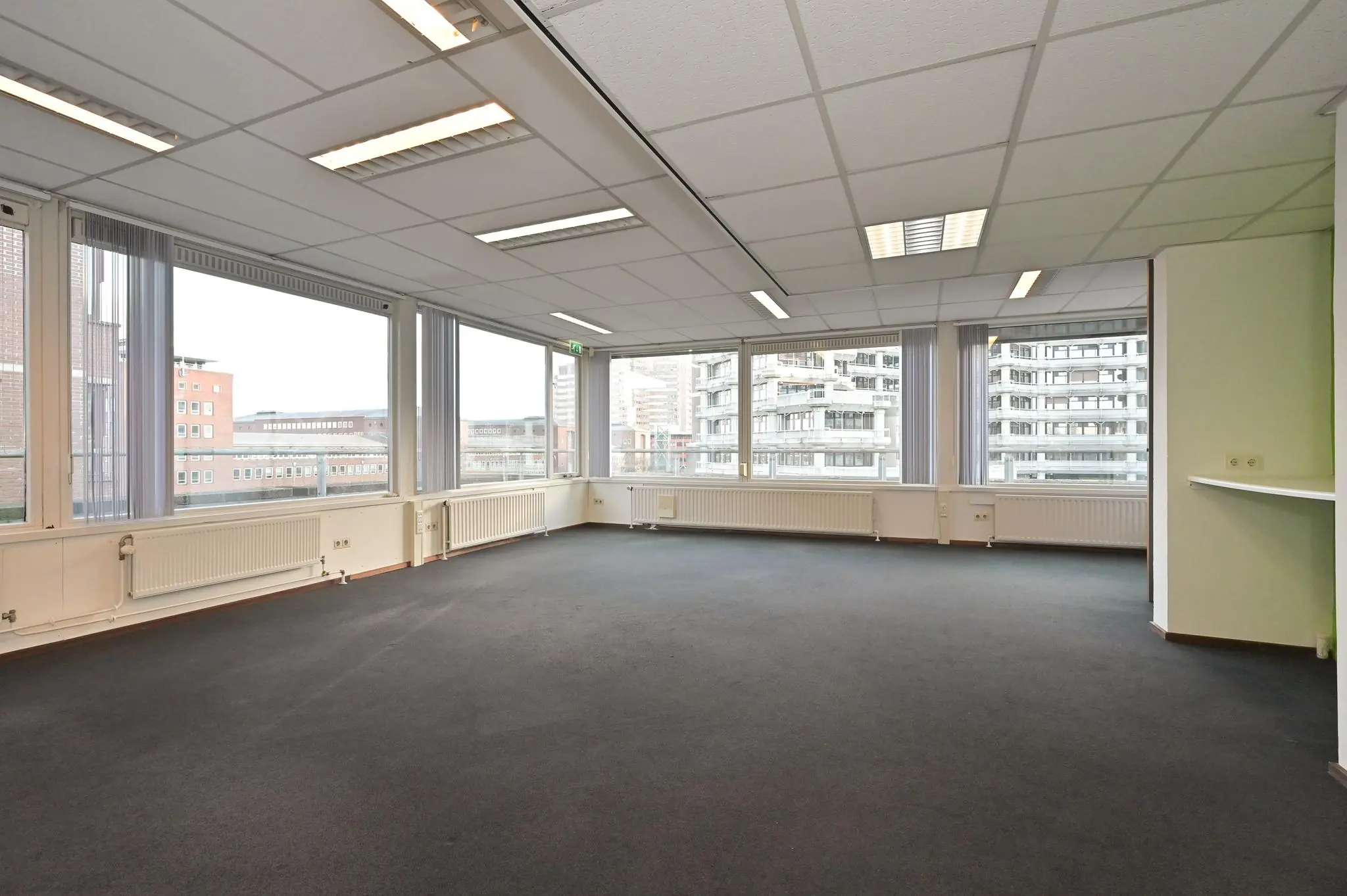 Licht en leeg kantoorruimte met tapijtvloer en grote ramen aan de Bezuidenhoutseweg.