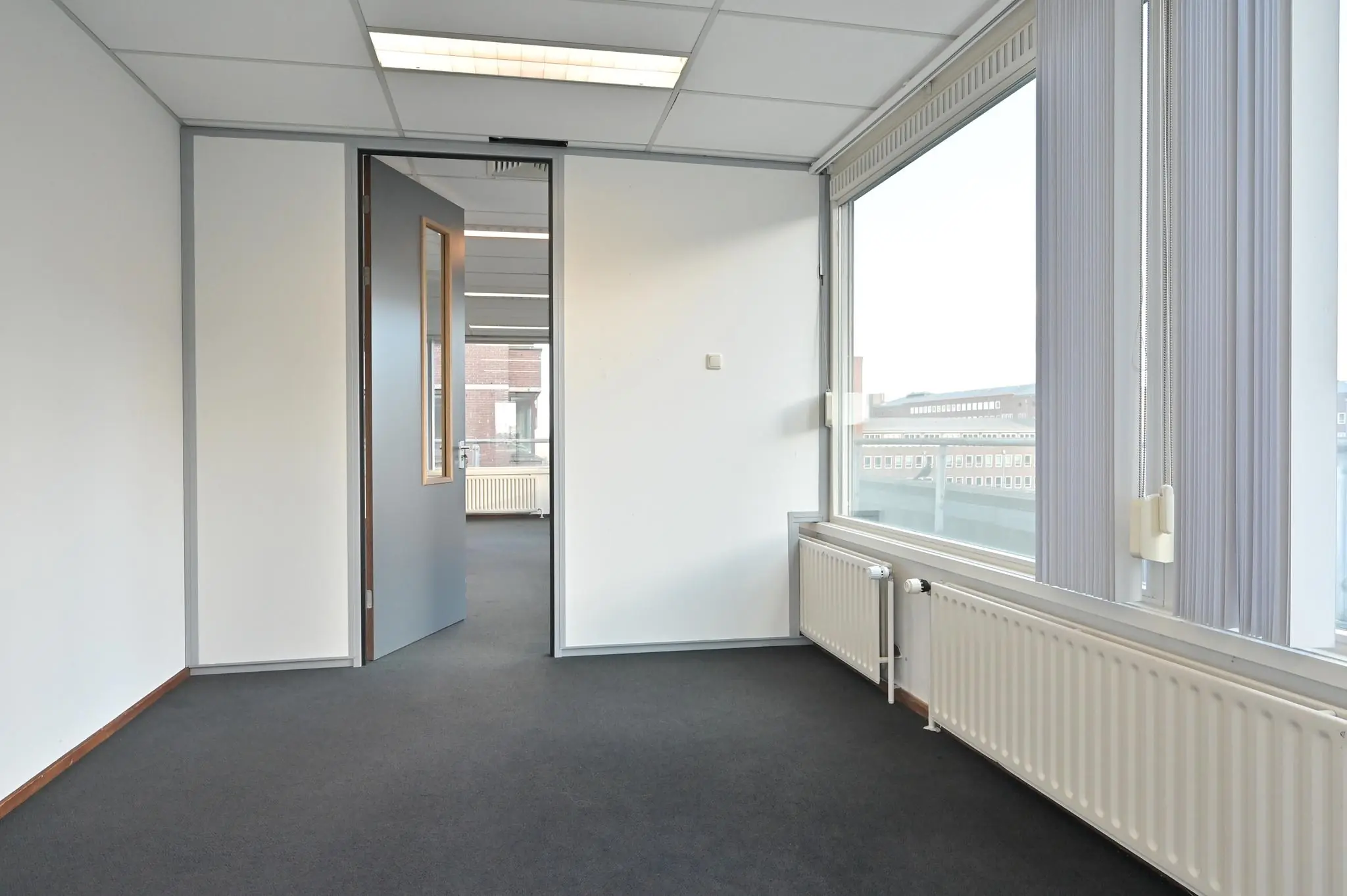 Leeg kantoorruimte aan de Bezuidenhoutseweg met grote ramen en zicht op omliggende gebouwen.