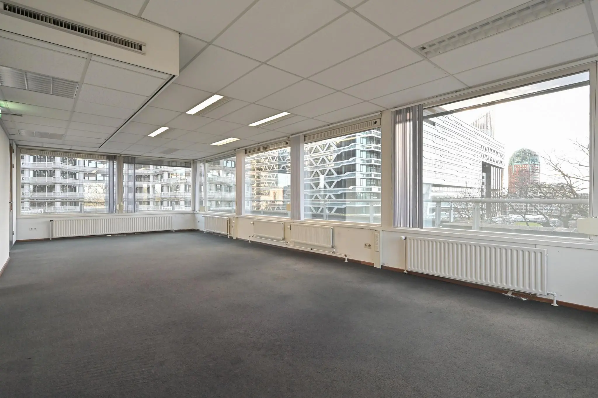 Licht en ruim kantoor met grote ramen aan de Bezuidenhoutseweg in Den Haag, met uitzicht op moderne kantoorgebouwen.