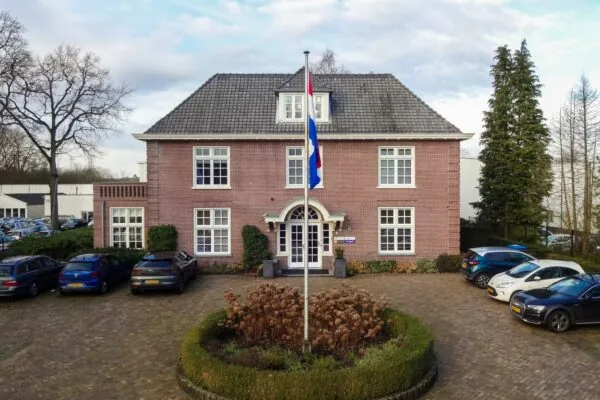 Vooraanzicht van een groot bakstenen kantoorpand aan de Amersfoortsestraat met Nederlandse vlag en geparkeerde auto's.