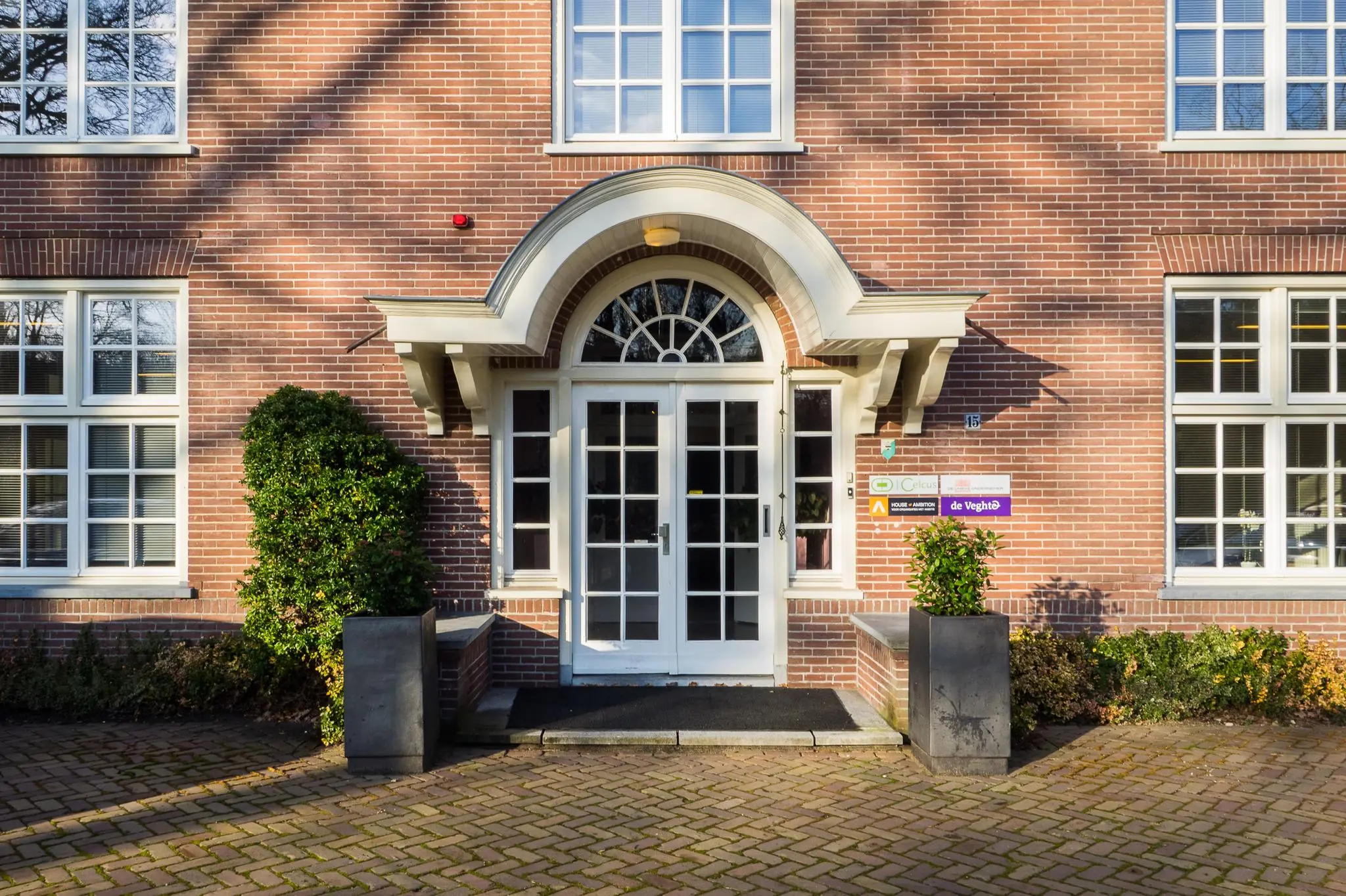 Vooraanzicht van het bakstenen kantoorpand aan de Amersfoortsestraat 15 met witte entree en naambordjes bij de deur.