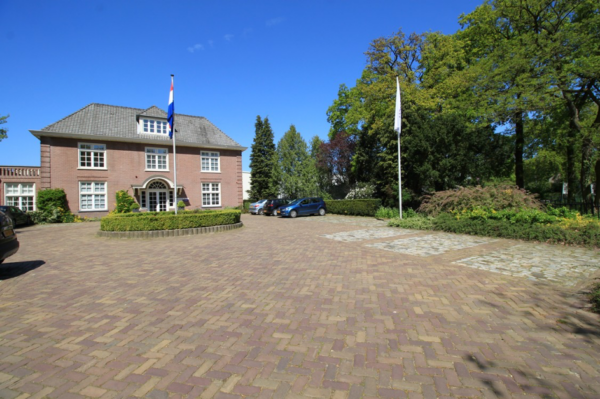 Vooraanzicht van een statig kantoorpand aan de Amersfoortsestraat met parkeerplaatsen en vlaggenmast op een zonnige dag.