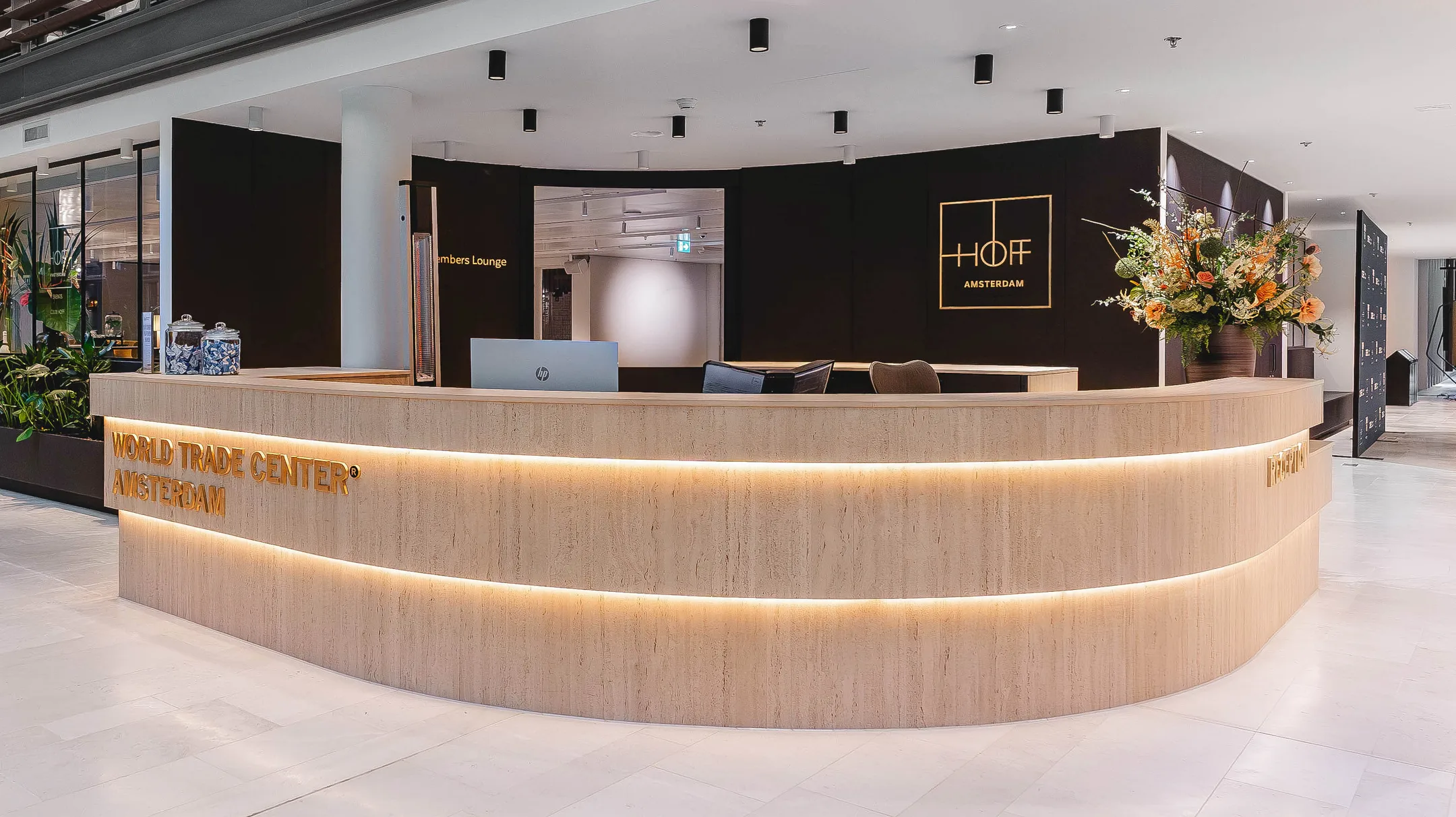De receptie van het World Trade Center Amsterdam met een ontvangstbalie, bloemenarrangement en verlichting.