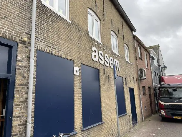Voorgevel van het pand van Van Assem aan de Molendijk met blauwe raamluiken en een geparkeerde rode vrachtwagen.