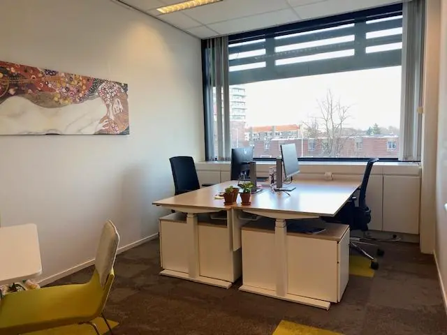 Kantoorruimte aan de Oudlaan met twee bureaus bij een raam, computers en een kleurrijk schilderij aan de muur.