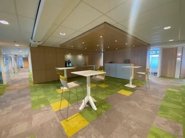 Moderne kantoorruimte aan de Oudlaan met hoge tafels, barkrukken en een koffiehoek op een kleurrijk tapijt.