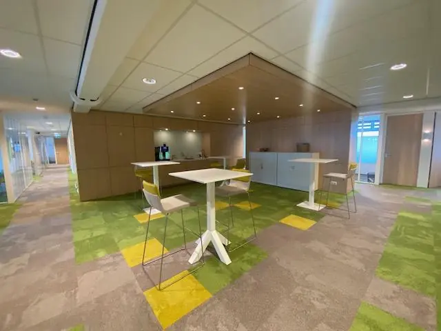 Moderne kantoorruimte aan de Oudlaan met hoge tafels, barkrukken en een koffiehoek op een kleurrijk tapijt.