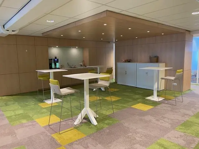 Moderne kantoorkeuken met statafels, barkrukken en een koffieautomaat op de Oudlaan.