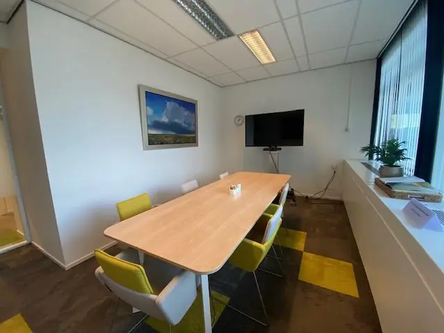 Vergaderruimte aan de Oudlaan met een lange tafel, zes stoelen, een tv-scherm en een schilderij aan de muur.