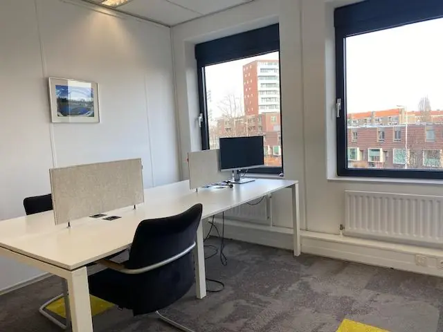 Lichte kantoorruimte aan de Oudlaan met twee werkplekken, bureaustoelen en uitzicht op omliggende gebouwen.