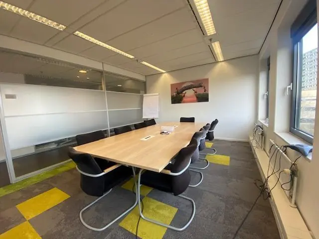 Vergaderruimte met een grote houten tafel, zwarte stoelen, een whiteboard en een kunstwerk aan de muur aan de Oudlaan.
