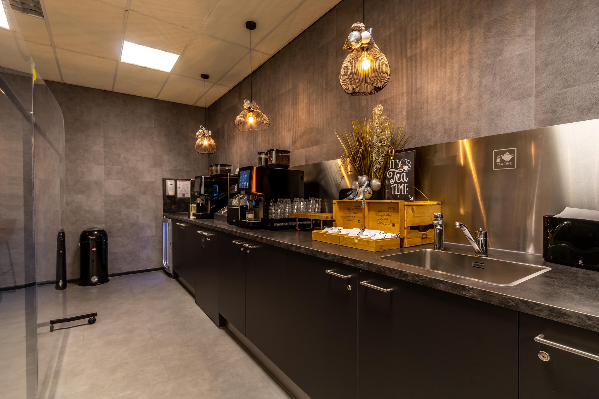Moderne pantry met koffiemachines, theekistjes en een spoelbak in een kantoor aan de Oudlaan.