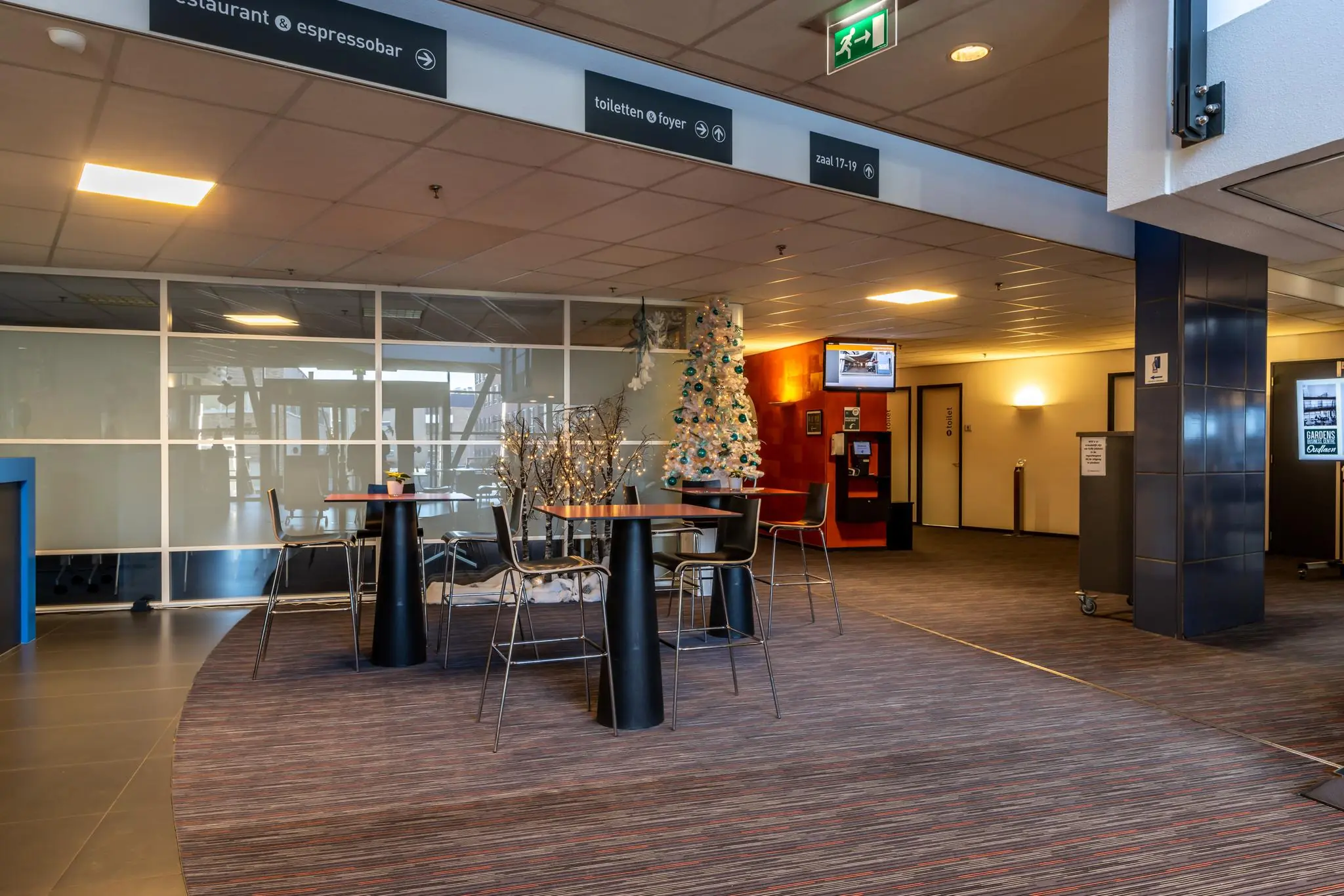 Moderne wachtruimte in een kantoor of openbaar gebouw met hoge tafels, stoelen en een versierde kerstboom.
