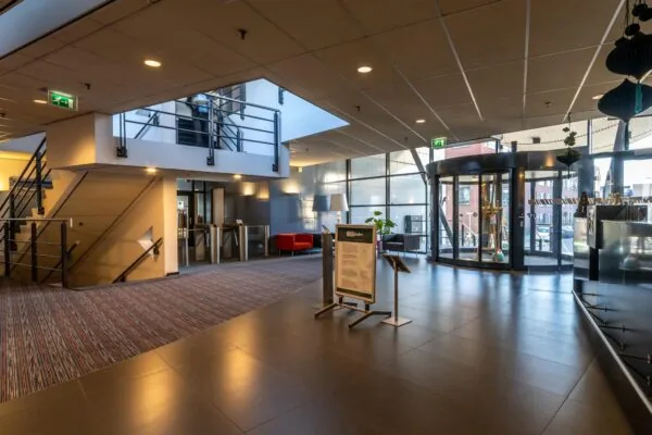 Moderne entreehal van een kantoorgebouw aan de Oudlaan met draaideur, informatiebord en trap naar boven.