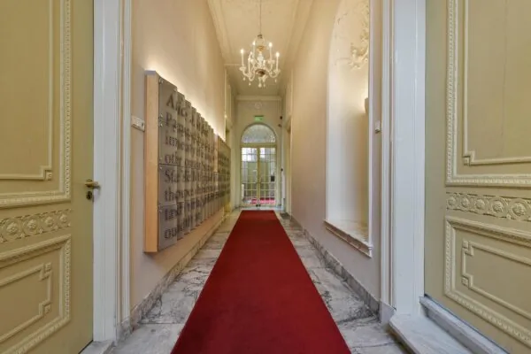 Luxe gang in een monumentaal pand aan het Rapenburg met een rode loper, marmeren vloer en sierlijke plafonddetails.